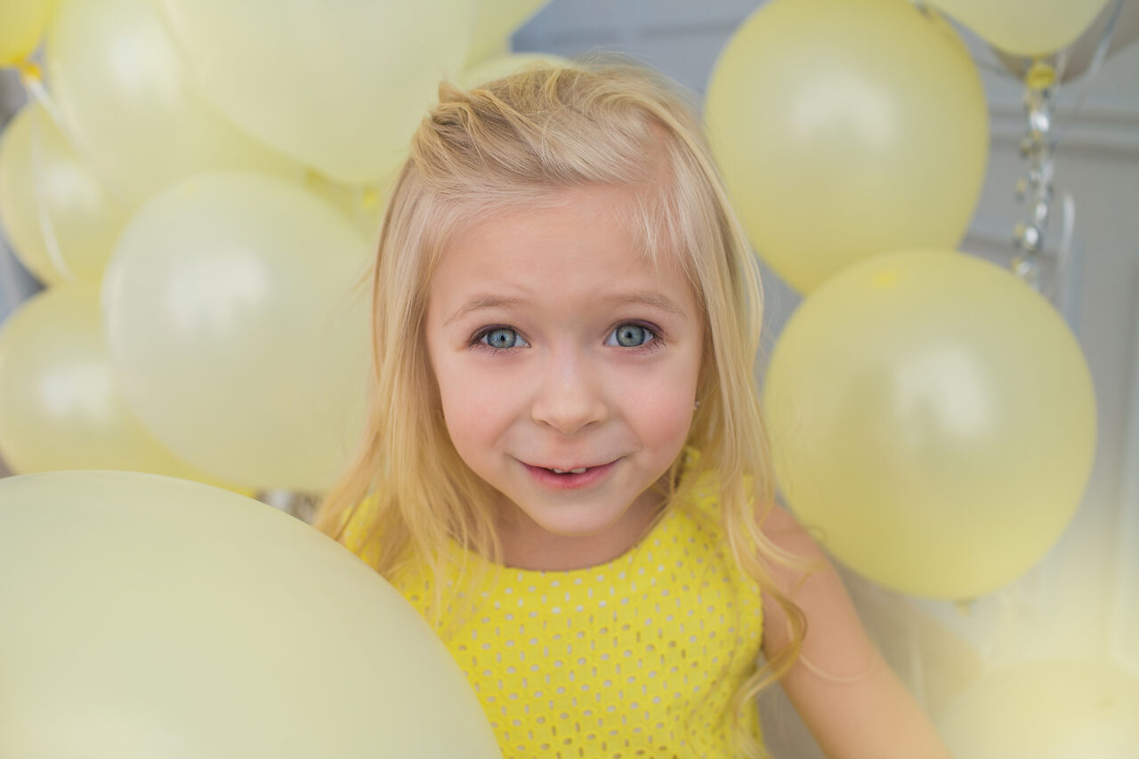 Portrait of a beautiful little girl in a yellow dress with a yellow balloons.