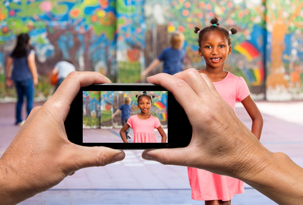 hands hold up a phone taking a picture of a little girl dancing