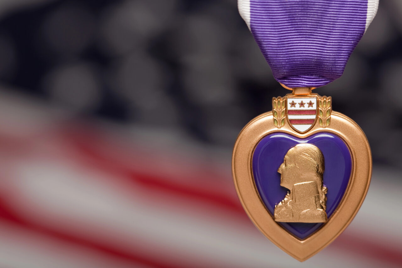 Purple heart medal hanging in front of U.S. flag.