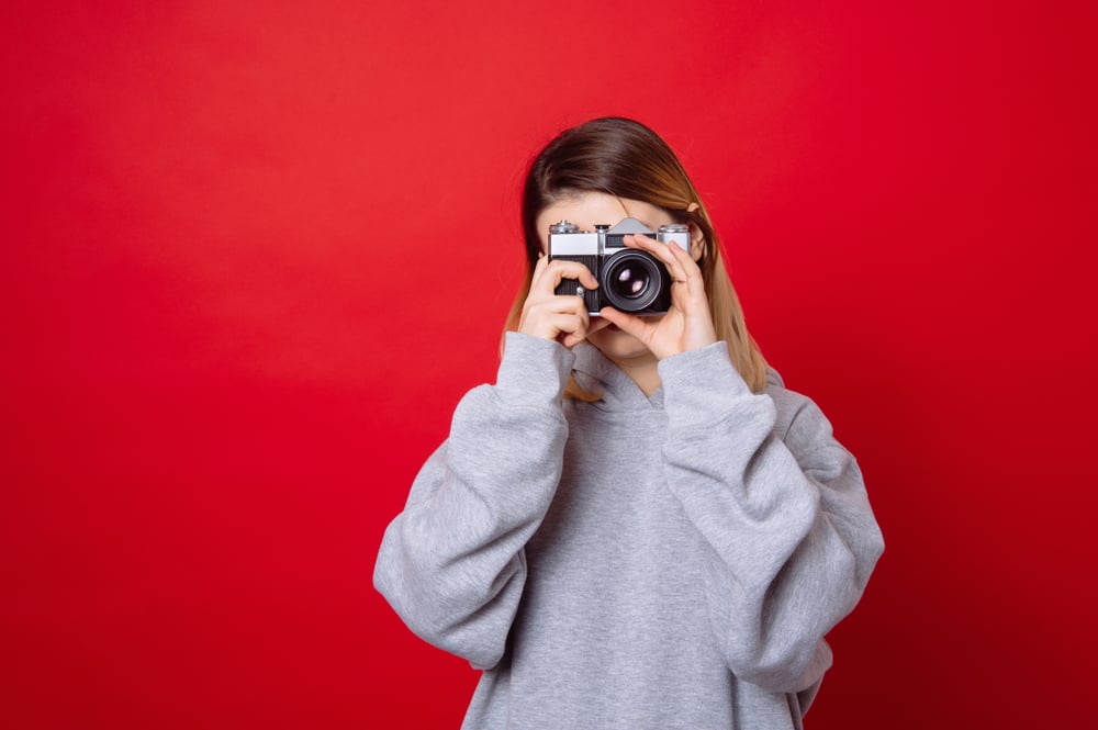 young woman holdin a camera standing against a red backdrop