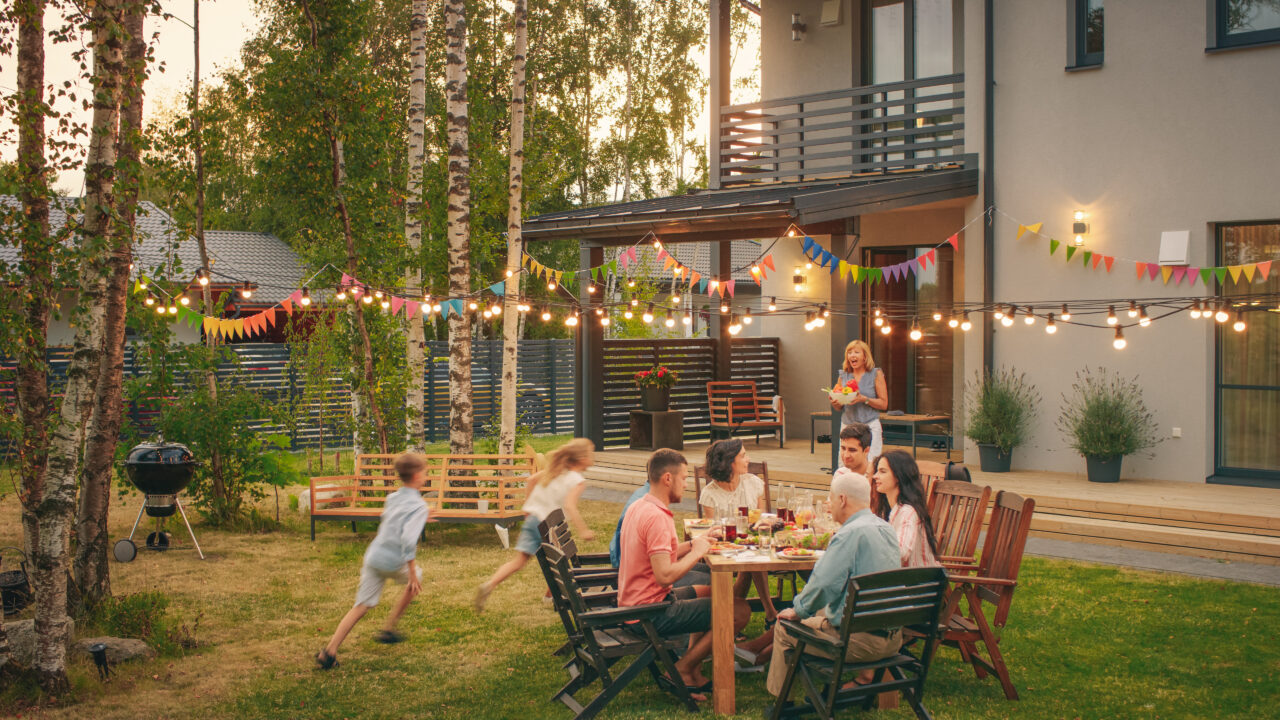 Family birthday party in a garden. People laughing and having dinner at table while kids run around.