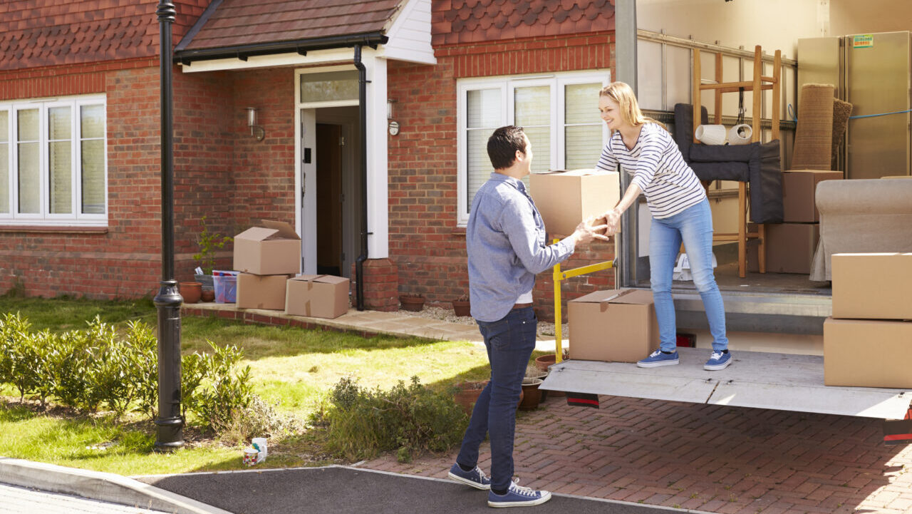 a woman handing a man a box from out of a moving truck.