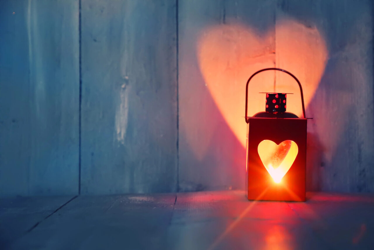 A lantern with a heart shape cut out glows in the dark.