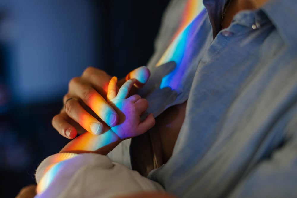 adult hand h0olding babies hand with rainbow of light over them