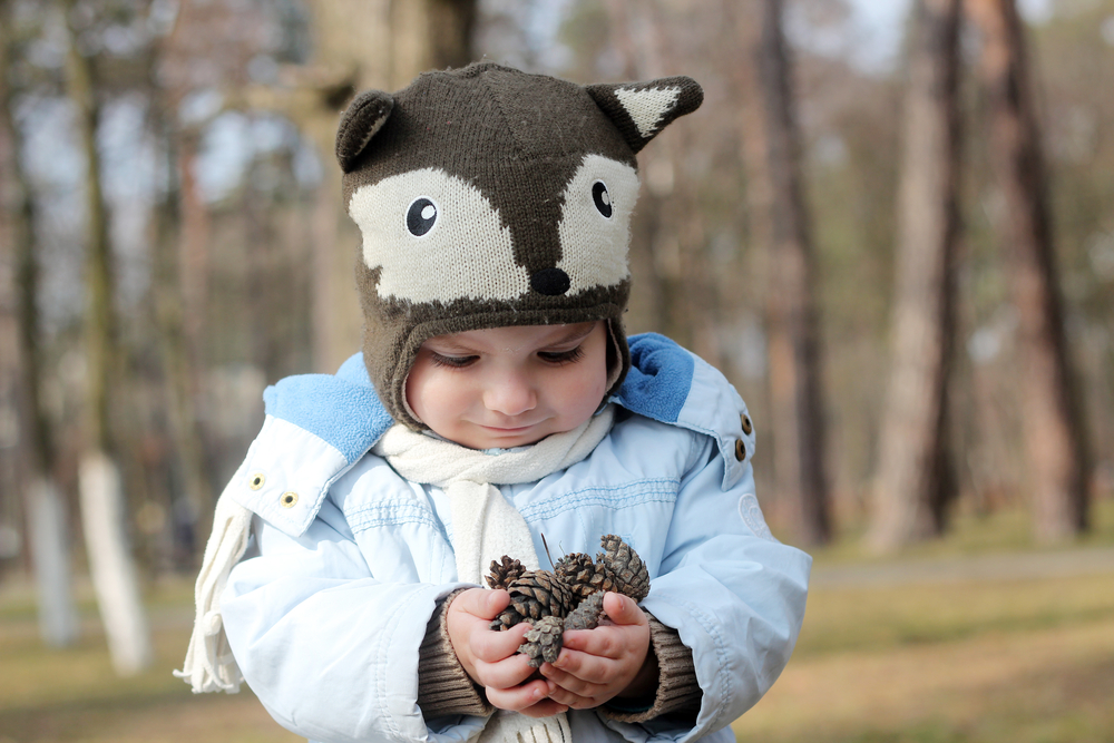 Toddler with wolf hat on stands in front of trees