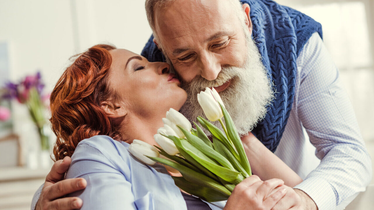 happy couple. older man giving his wife flowers while she kisses him on the cheek.