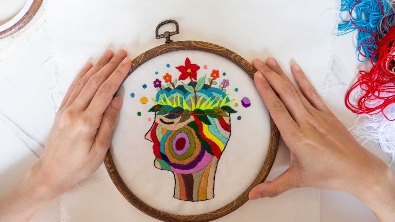 Hand embroidery of beautiful creative art of colorful head with flowers growing at the top.