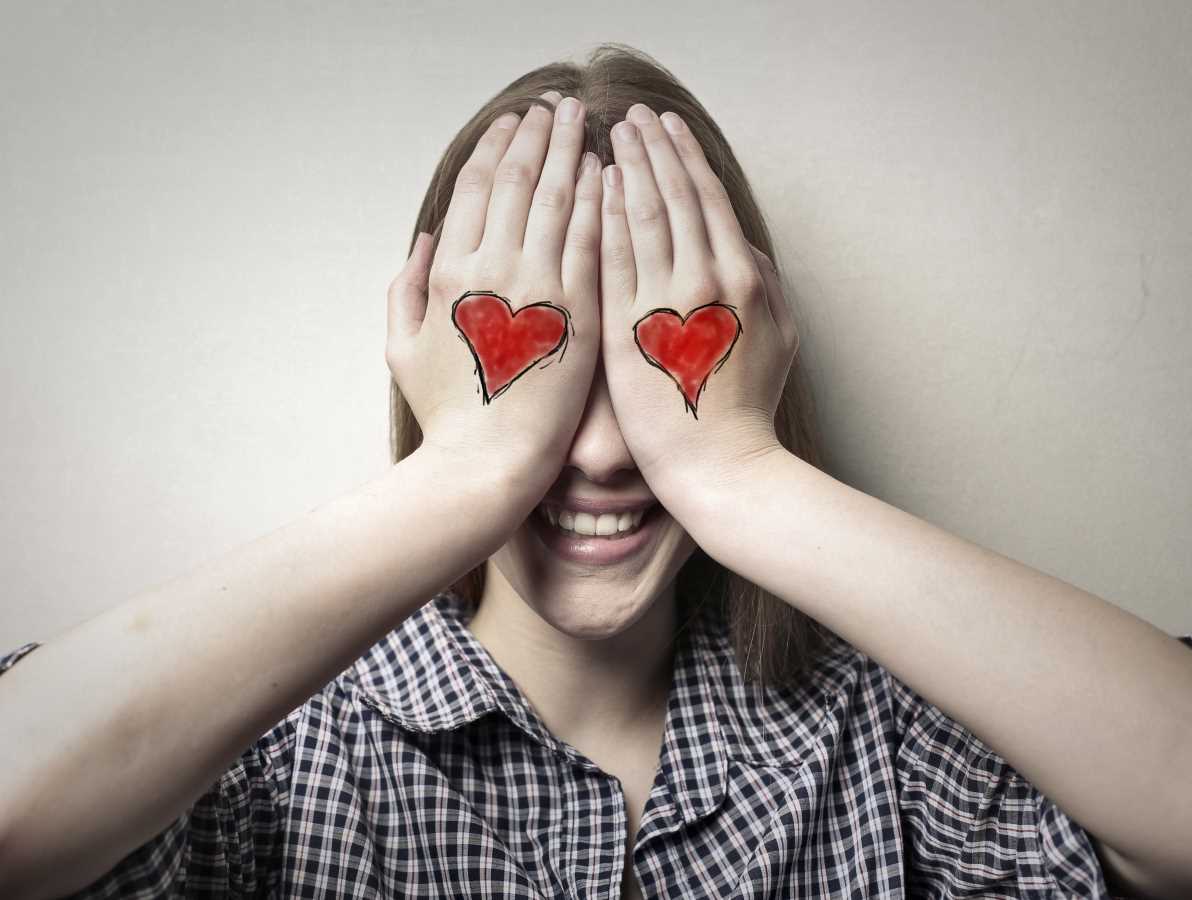 person with hearts drawn on their hands covers their eyes so the hearts look like eyes.