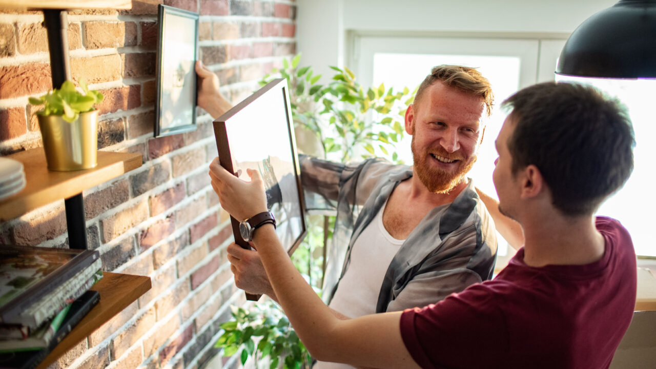 Happy gay couple hanging photos in home.