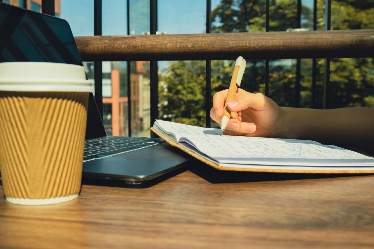 Young woman study at wooden table in shopping mall food court. Drinking coffee from paper cup.