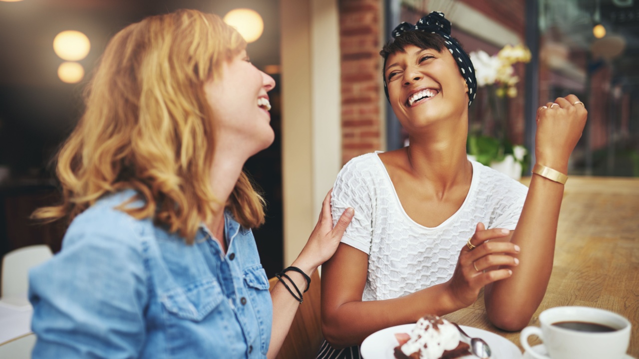 Two friends at a restaurant laughing together.