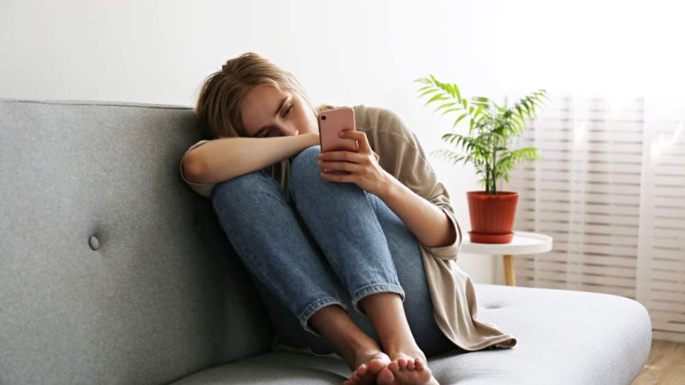 Sad-young-woman-curled-on-couch-with-phone