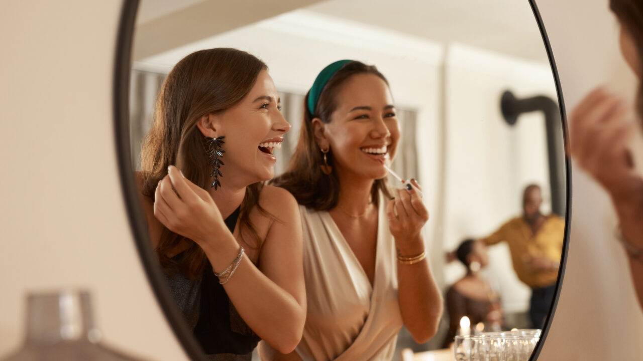 Friends laughing in mirror while getting ready.