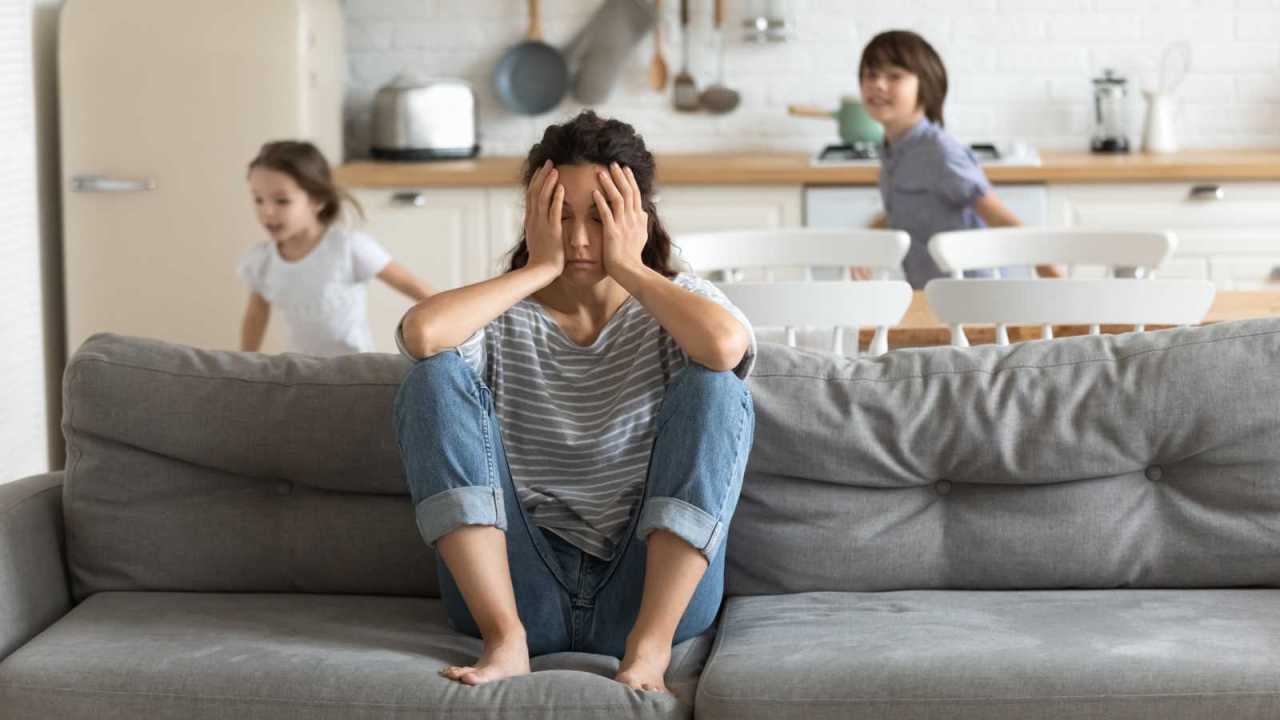 tired upset mom on couch with hyper children running around her.