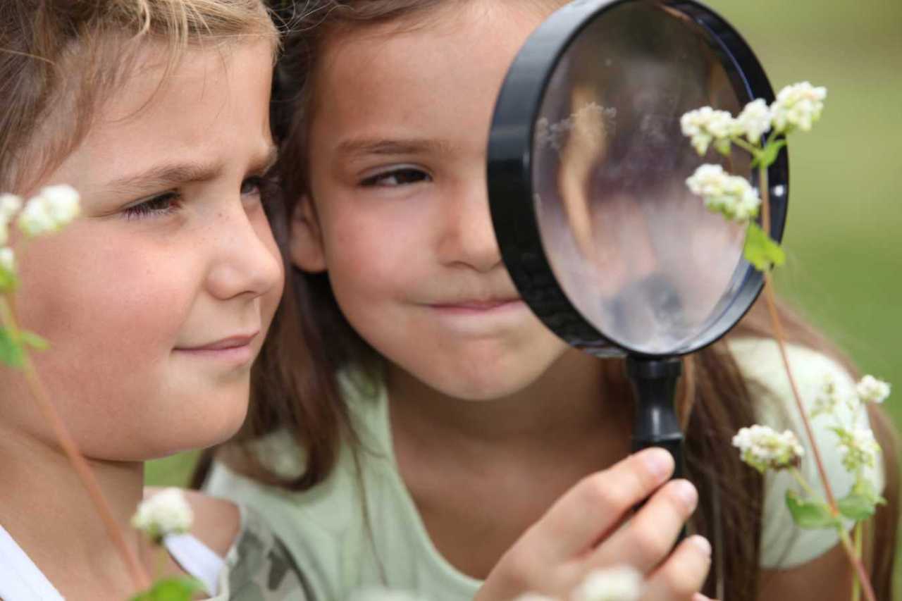 two kids look through magnafying glass at a plant.